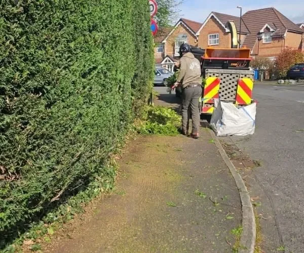 Two Highfield tree surgeons in high-visibility orange safety gear using chainsaws to clear a large fallen tree trunk in a residential garden in Urmston following Storm Lilian.